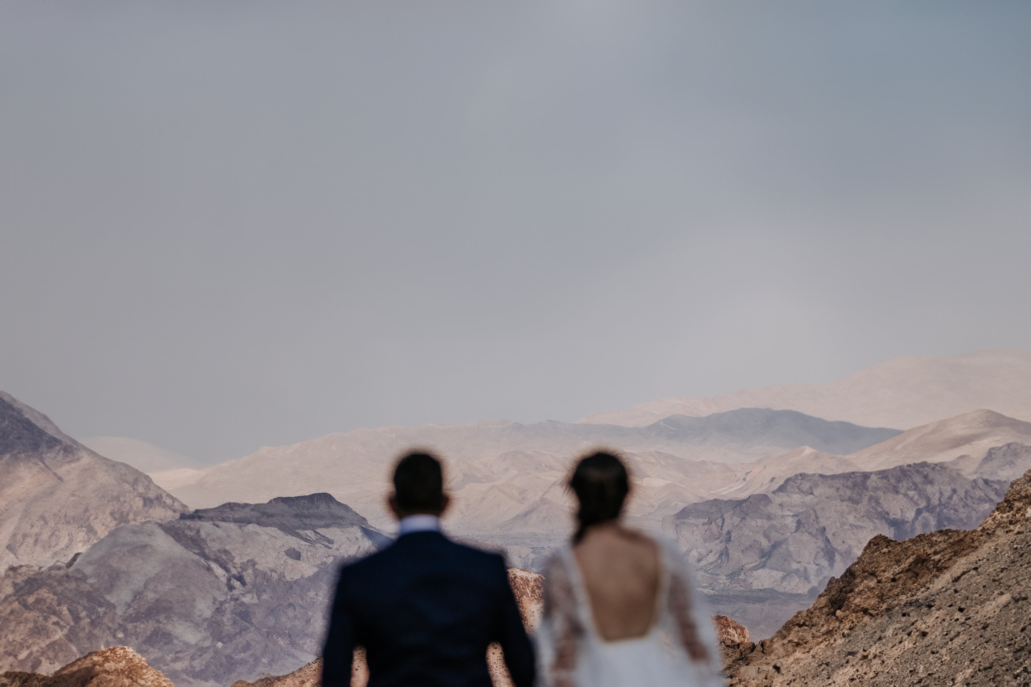 A bride and groom stand in the foreground, out of focus, looking toward a large, pastel desert canyon outside of Las Vegas, NV