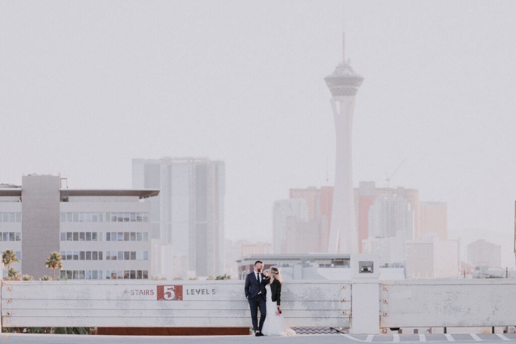 A wide shot of a newlywed couple standing on the rooftop of a parking garage with the Stratosphere and the Strip prominent in the background in Las Vegas.