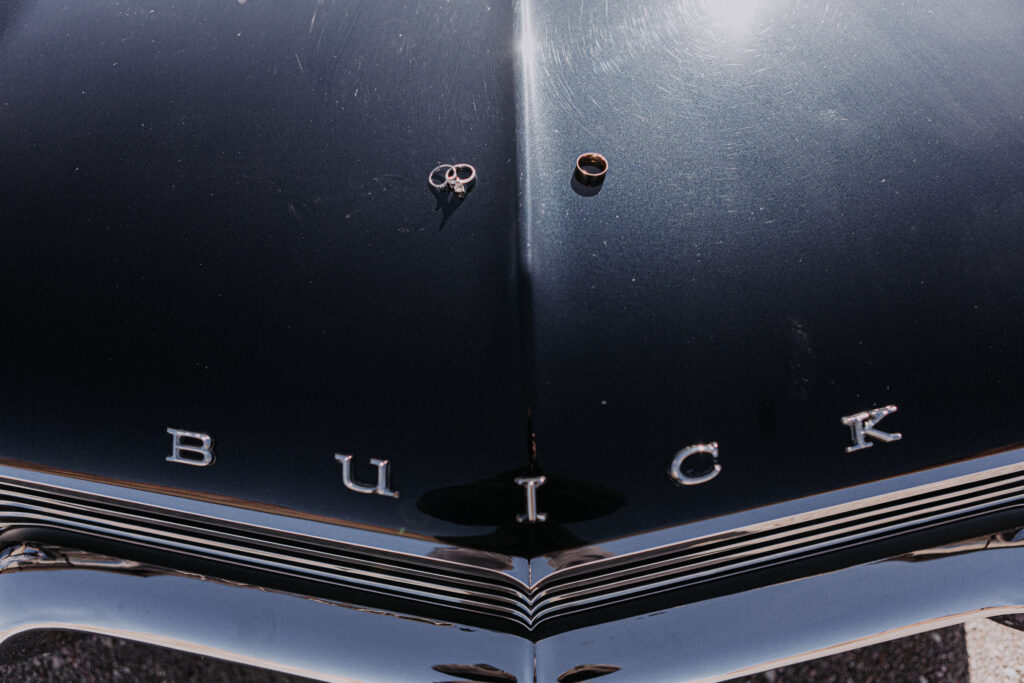 wedding rings sit atop the hood of a vintage black Buick car.