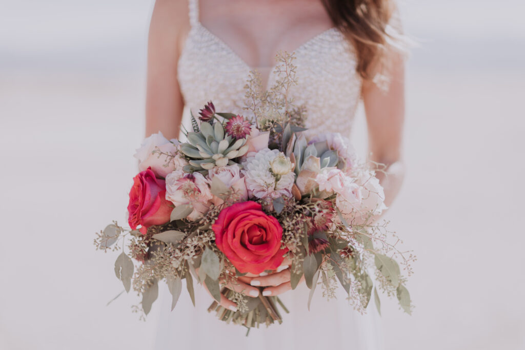 A bride holes a colorful bouquet, accented with bright fuschia flowers.