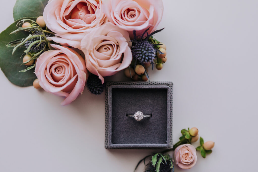 a flat-lay image of a ring box surrounded by pale pink roses.