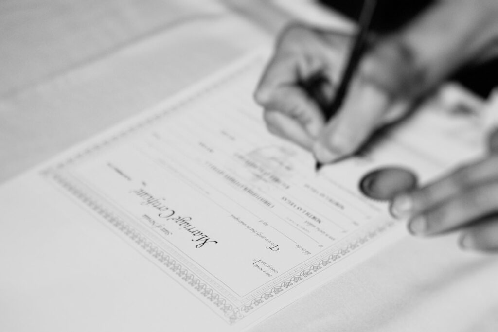 An up-close image of a witness' hand signing a marriage license.