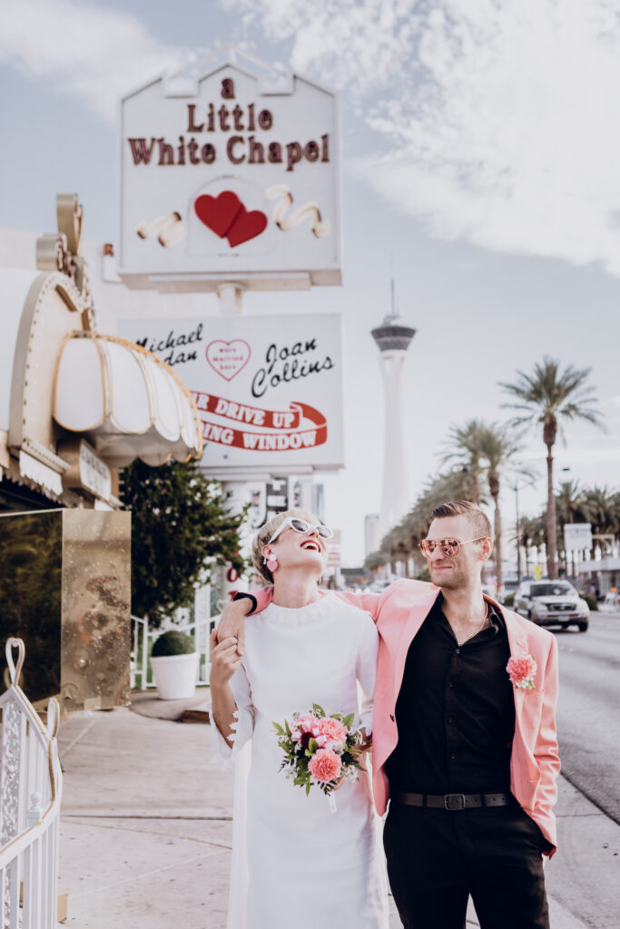 bride and groom celebrate and laugh while walking to the Vegas Strip after wedding at a drive-thru wedding chapel.
