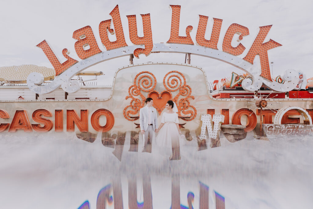 A bride and groom stand side-by-side in front of the Lady Luck sign at the Neon Museum in Las Vegas.