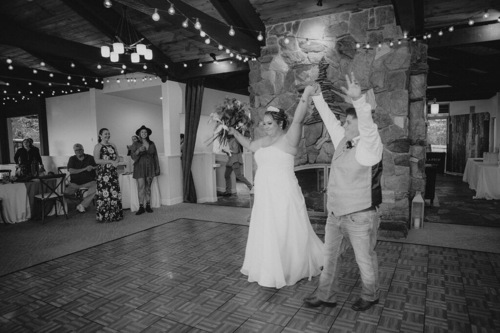 A couple enters their reception on a dance floor with a double-side stone fireplace in the background.