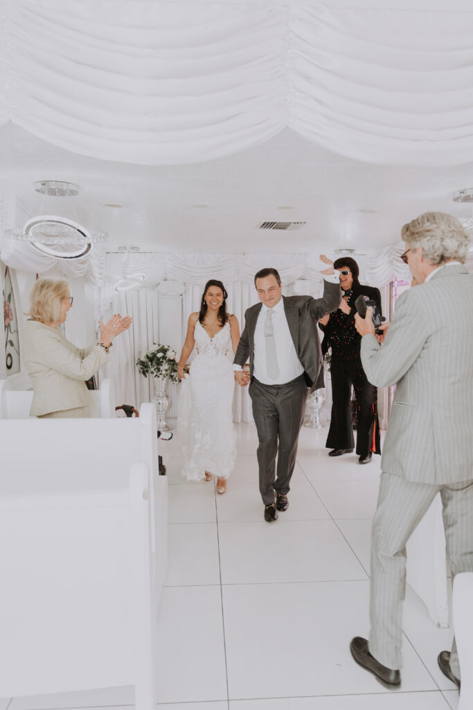A newly married couple walks down the aisle of a small, white wedding chapel after being wed by Elvis in Las Vegas.